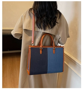 Detail of color-block denim tote bag showing leather handles and shoulder strap on model
