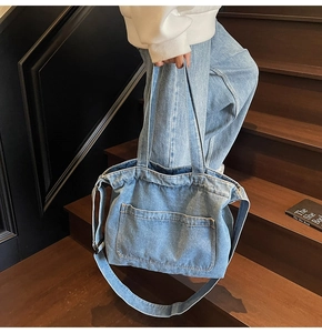 Detail of light blue denim tote bag featuring large front pocket and wide shoulder strap