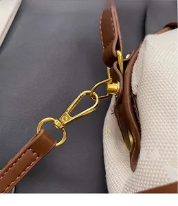 Detail of gold hardware hook and brown leather strap on a canvas monogram handbag