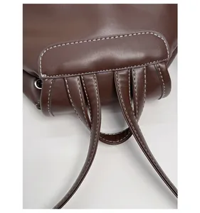 Detail of reinforced stitching and brown leather texture on the backpack strap connector