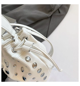 Detailed side view of white bucket bag with large silver rivets and drawstring closure