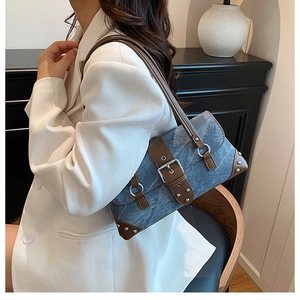 Detail view of denim shoulder bag with leather trim, buckle, and silver rivets