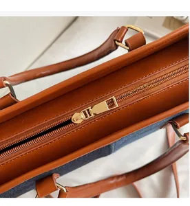 Detail of the smooth gold metal zipper and brown leather trim on the denim tote bag