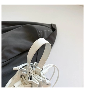 Detail of white bucket bag featuring silver hardware rings and a sleek drawstring closure