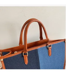 Detail of blue canvas tote bag with brown leather handles and gold metal zipper
