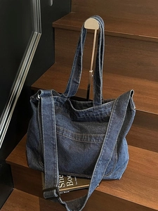 Deep blue denim tote bag with adjustable strap displayed on stylish wooden stairs