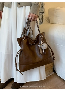 Detail of retro brown tote bag featuring side drawstrings and eye-shaped plush pendant