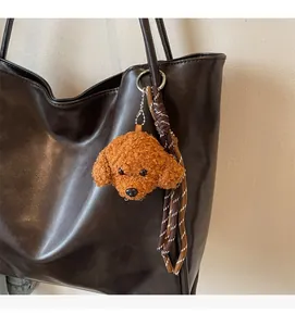 Detail of cute brown teddy dog plush pendant with woven lanyard on a leather tote bag