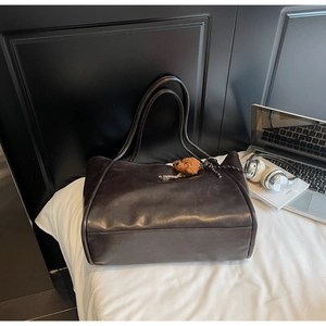 Detail of a dark brown tote bag with a teddy bear charm and soft leather texture