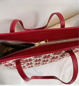 Détail de la fermeture éclair dorée et des poignées en cuir rouge du sac cabas