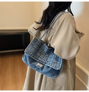 Detail of light blue quilted denim shoulder bag with silver chain strap on a trench coat