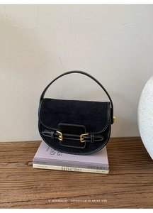 Detail of black suede saddle bag with white contrast stitching and gold buckles
