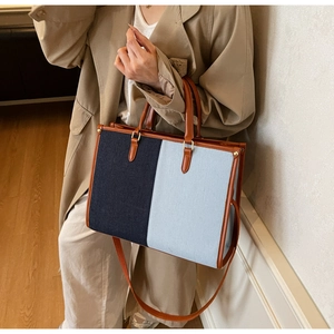 Detail of blue canvas tote bag with brown leather trim held by model in trench coat