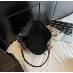 Macro view of a dark leather tote bag's spacious interior with a brown teddy bear charm