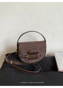 Detail of a brown leather saddle bag with contrast stitching and gold metal buckle