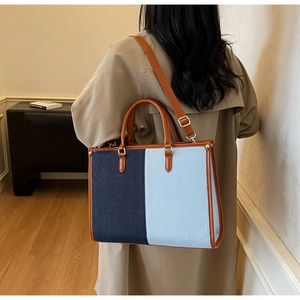 Detail of contrast stitch denim tote bag with leather straps on a model wearing a trench coat