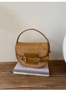 Close-up of tan saddle bag featuring suede texture and gold metallic buckle details