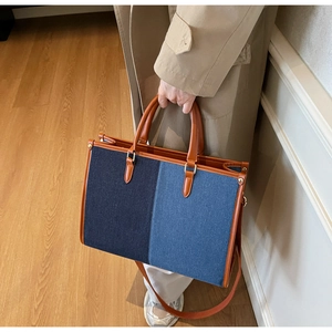 Close-up of a two-tone denim tote bag featuring brown leather trim and gold metal accents