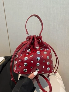 Red patent leather bucket bag featuring silver stud rivets and a drawstring closure