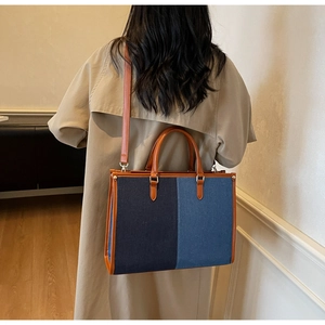 Detail of color-block denim tote bag featuring brown leather trim and detachable shoulder strap