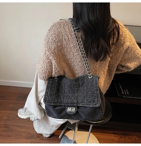 Detailed view of large quilted denim chain bag with silver lock on a model's shoulder