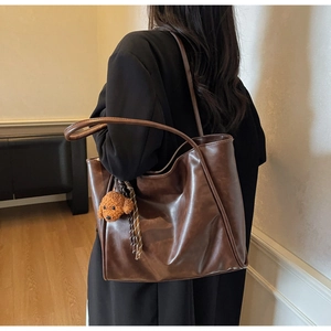 Detail of dark brown oil wax leather tote bag with a cute puppy charm and plaid ribbon
