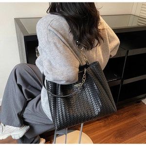 Detailed close-up of the woven texture and fashion metal logo on the black tote bag