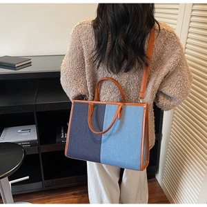 Detail of blue denim patchwork tote bag with brown leather handles on shoulder