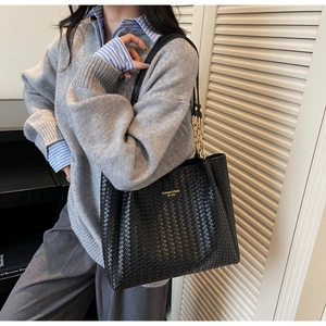 Detail of black woven leather tote bag with gold chain strap and metal logo on a model
