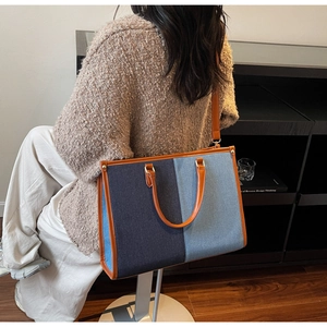 Detail of contrast stitch tote bag featuring premium denim texture and brown leather trim