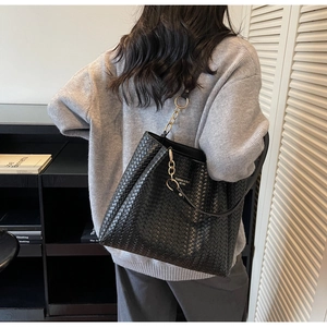 Detail of a black woven tote bag with gold chain strap on a model's shoulder