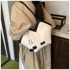 Detail of beige canvas tote bag featuring V-shaped opening and black woven branding strap