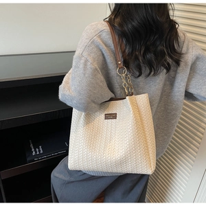 Detail of woven tote bag featuring brown leather and gold chain shoulder straps