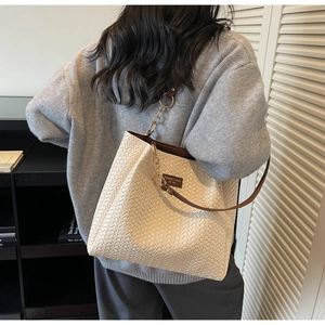 Detail of cream woven tote bag showing leather strap with gold chain links