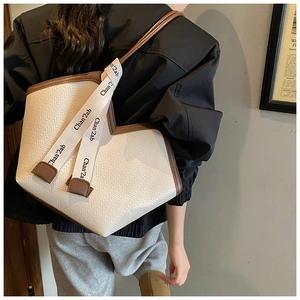 Detail of cream woven tote bag featuring brown leather trim and unique V-shaped top line