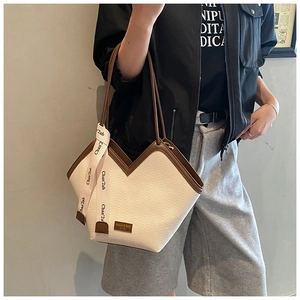Close-up of beige woven tote bag with brown leather trim and decorative printed silk scarf
