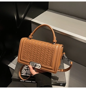 Détail de la texture en cuir tressé marron et du fermoir rotatif doré du sac à main