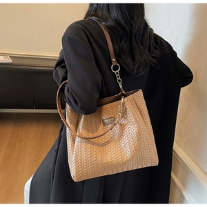Detail of light brown woven tote bag with leather strap and gold chain on model