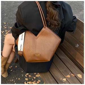 Close-up of textured brown leather tote bag with V-shaped opening and branding detail