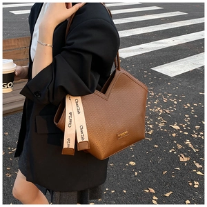 Close-up of brown textured leather tote bag with V-shaped opening and lettered strap