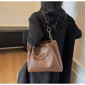 Macro detail of dark brown woven leather tote with gold chain and refined texture