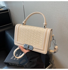 Détail du sac bandoulière tressé crème avec fermoir argenté et structure accordéon