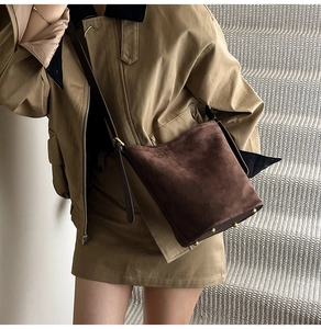 Detail of brown suede bucket bag featuring protective base rivets and adjustable strap