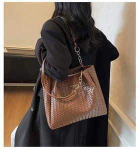 Brown woven tote bag with gold chain strap detail shown on model's shoulder