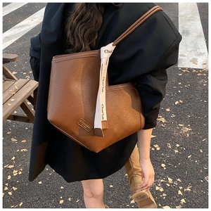 Close-up of brown wavy embossed tote bag with beige ribbon detail on street model