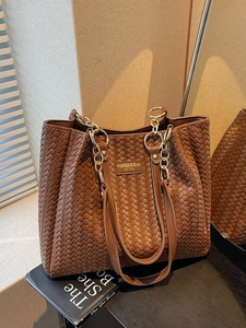 Brown woven tote bag with dual handles and gold chain strap in a luxury setting