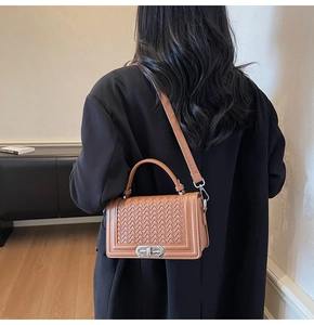 Sac bandoulière marron tressé avec fermoir rotatif argenté porté sur l'épaule d'un mannequin