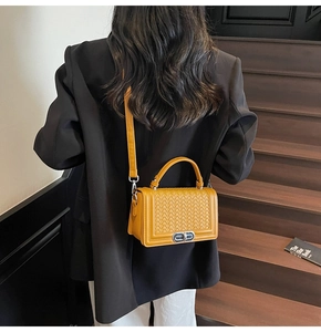 Détail d'un sac carré tressé jaune gingembre porté avec un blazer noir élégant