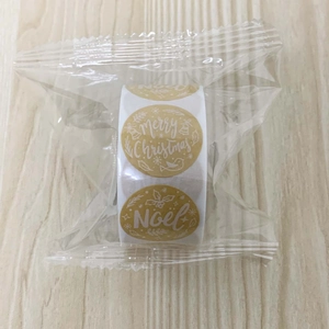 Macro detail of Merry Christmas gold round roll stickers inside transparent plastic packaging