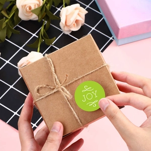 Green Christmas JOY round adhesive labels on kraft paper gift box with twine decoration
